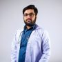 Portrait of a bearded male doctor in a white coat with a stethoscope in a studio setting.